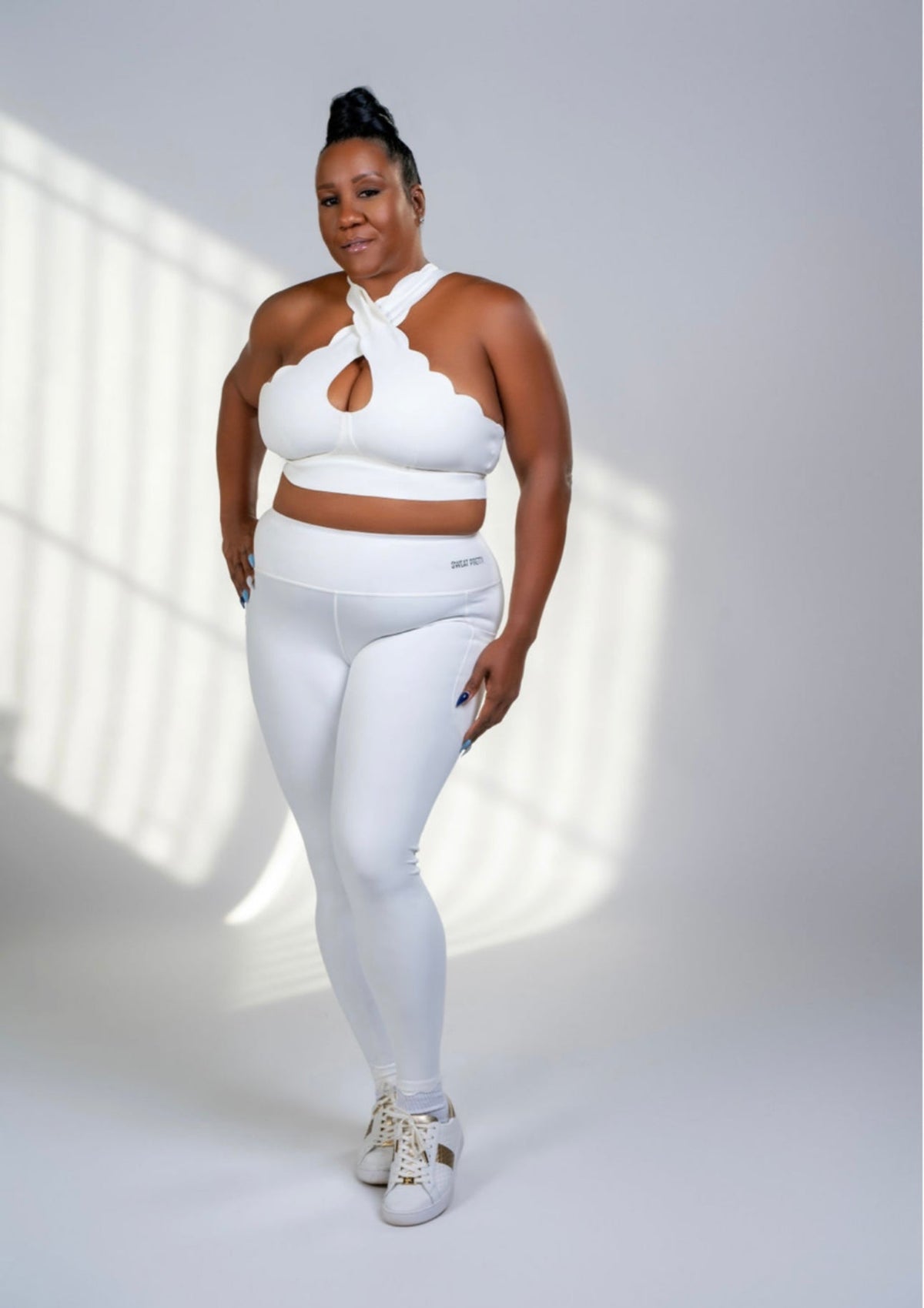 Person wearing a white outfit with a halter top and leggings on a light background