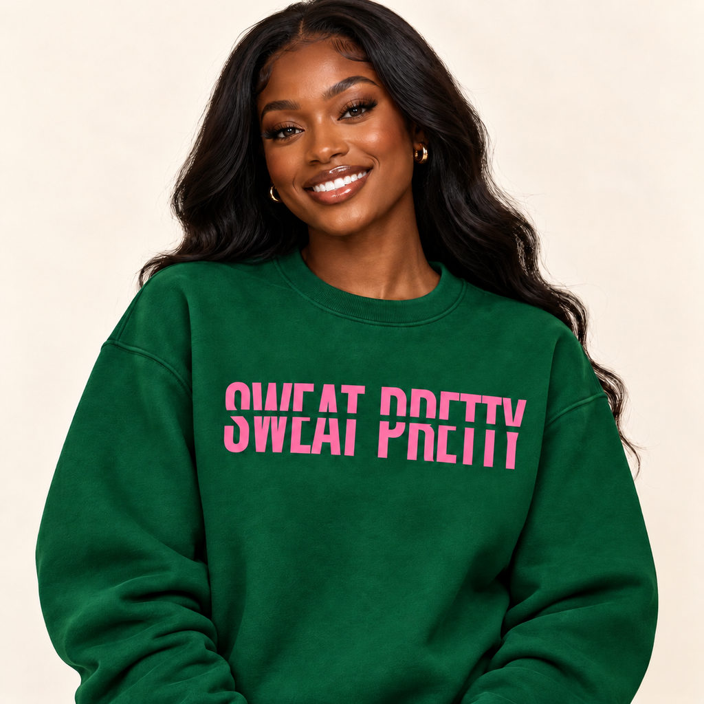 A woman with long dark hair wearing a green crewneck sweatshirt with the text 'SWEAT PRETTY SWEAI PRETTY' printed in pink across the chest, set against a plain beige background.