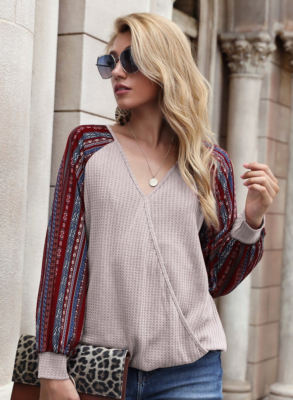 Woman wearing a patterned cardigan over a beige top with sunglasses and a clutch.