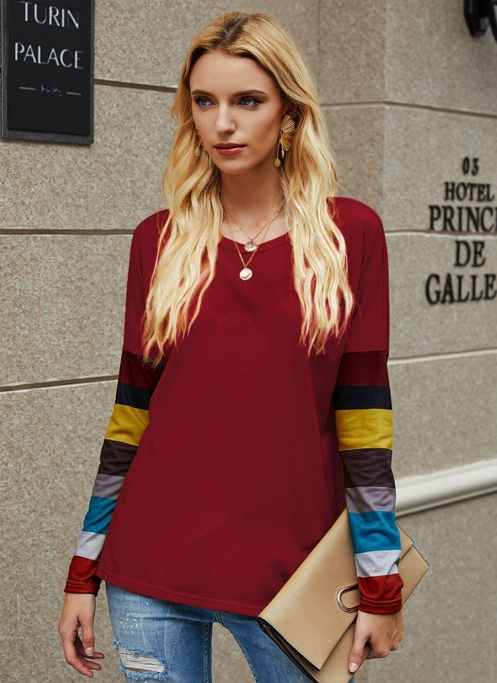 Woman wearing a red long-sleeve top with colorful sleeves against a stone wall.
