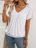 A woman wearing a white short-sleeve V-neck top with a gathered neckline, paired with blue jeans, shown in a styled indoor setting.