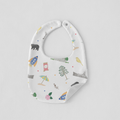 A white baby bib with a colorful whimsical print of rockets, a circus tent, a tree, a bird, and stars, shown on a light gray background.