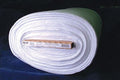 A roll of white fabric with a cardboard label wrapped around the center, photographed against a dark blue and black background.