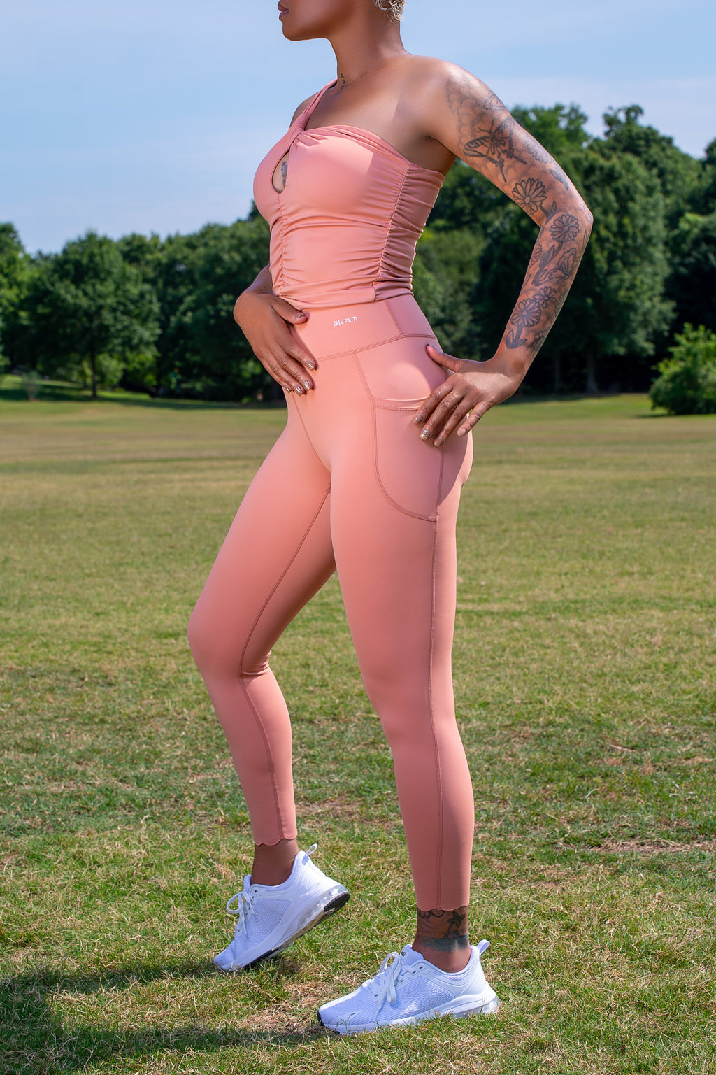Person wearing a pink athletic outfit standing in a grassy field with trees in the background
