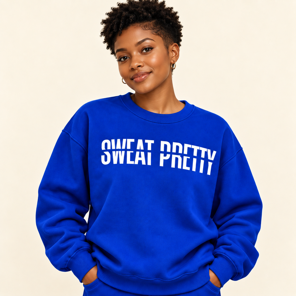 A woman wearing a bright royal blue sweatshirt with the phrase 'SWEAT PRETTY' printed in bold white letters across the chest, posed against a solid light beige background.