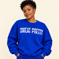 A woman wearing a bright royal blue sweatshirt with the phrase 'SWEAT PRETTY' printed in bold white letters across the chest, posed against a solid light beige background.