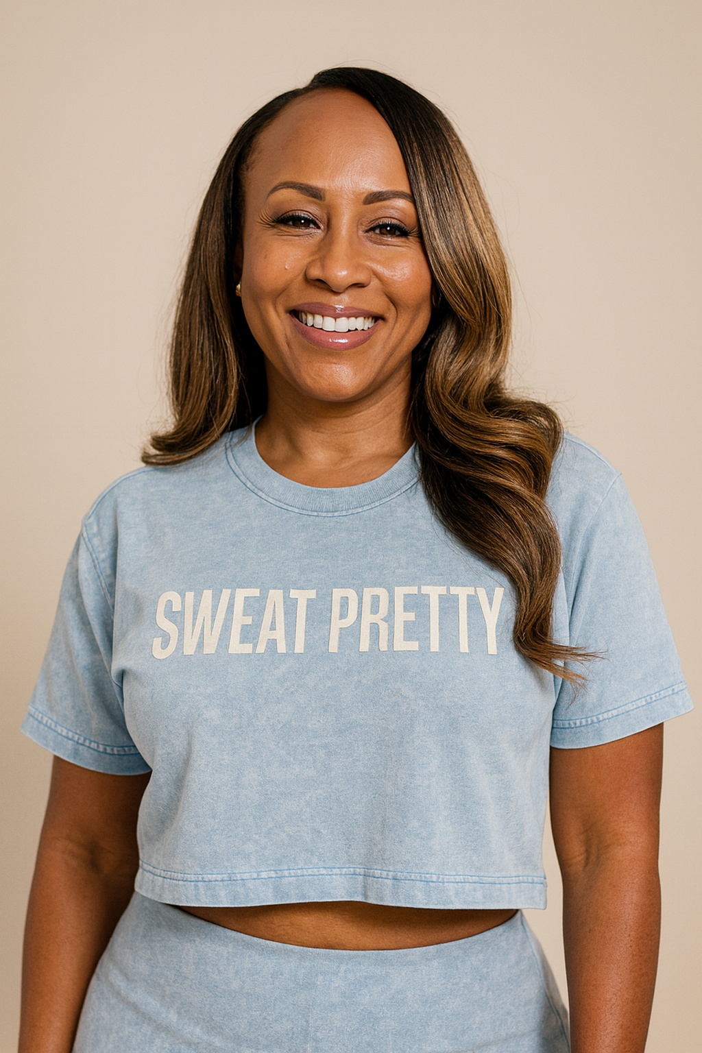 Woman wearing a light blue 'SWEAT PRETTY' t-shirt against a beige background