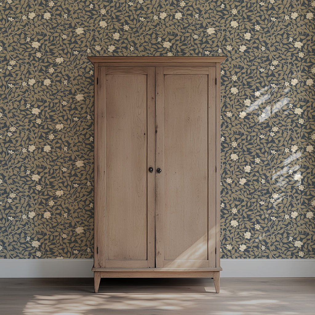A tall light oak double-door wardrobe or armoire stands against a dark floral wallpapered wall in a room with a light wood floor. The cabinet has two doors with small round black knobs and is photographed from the front.