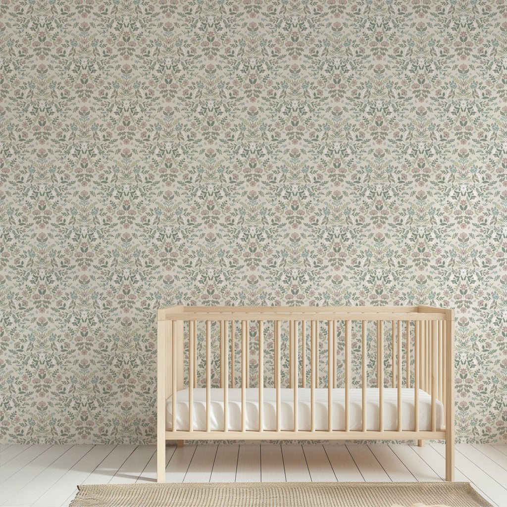 A light natural wood crib with a white mattress placed in front of a wall covered in an intricate, repeating botanical damask wallpaper pattern.