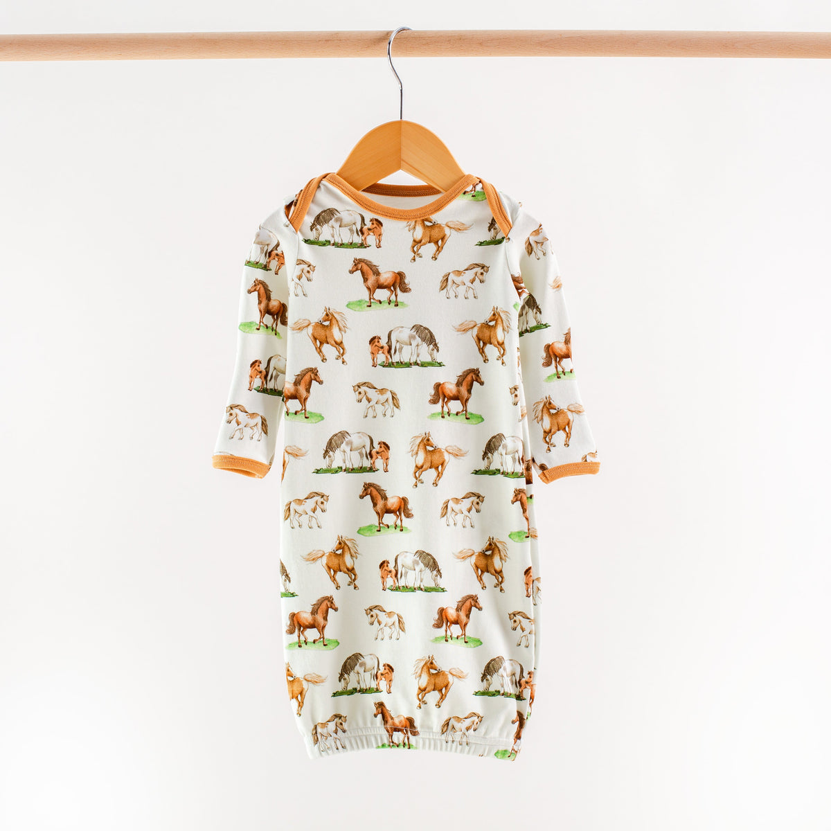 Baby onesie with horse pattern on a hanger against a white background