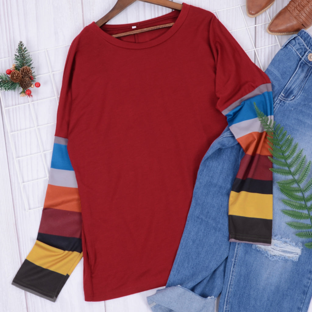 Red long-sleeve shirt with colorful sleeves on a hanger next to blue jeans.