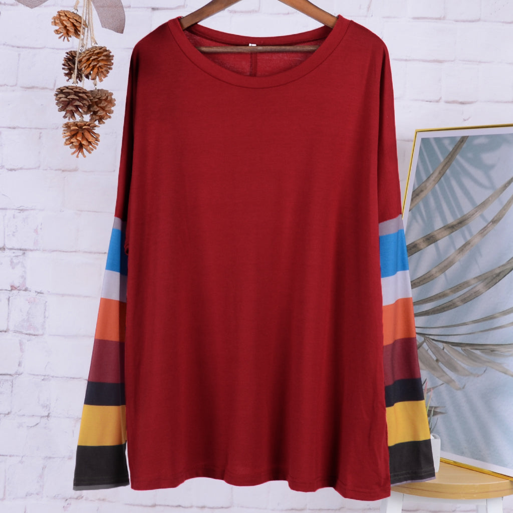 Red dress with colorful stripes on a hanger against a white brick wall.