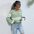 Woman wearing a green and white striped sweater and blue jeans, holding a coffee cup against a light background.