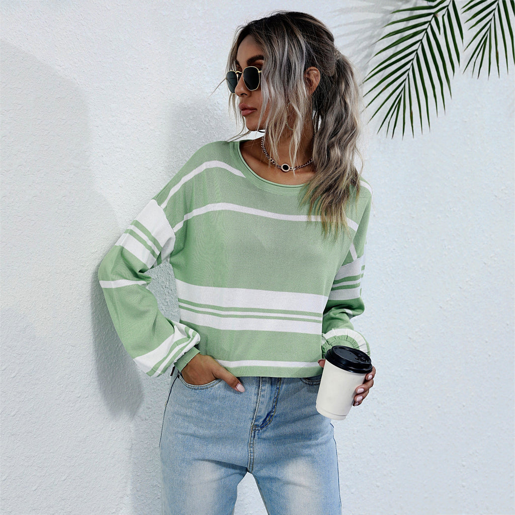 Woman wearing a green and white striped sweater and blue jeans, holding a coffee cup against a white background with a leafy plant.