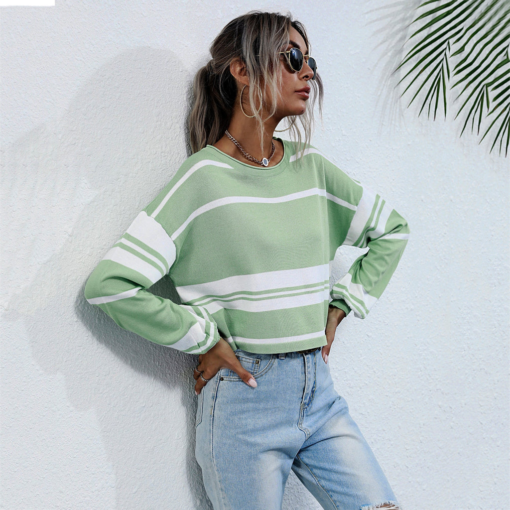 Woman wearing a green and white striped sweater and blue jeans against a light background