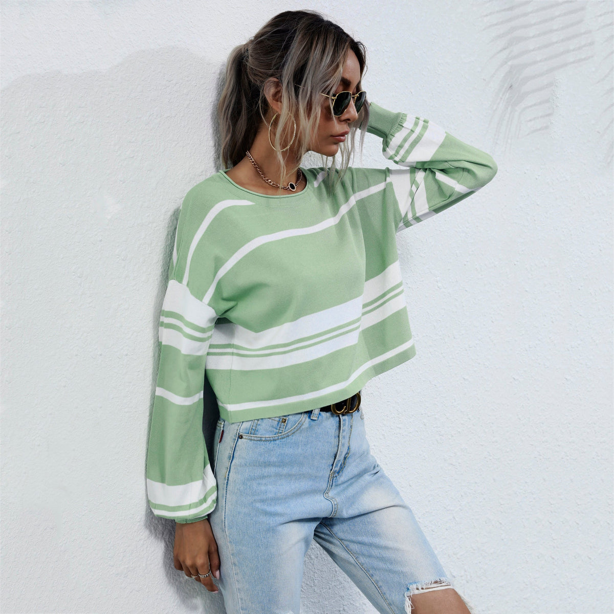 Woman wearing a green and white striped sweater and blue jeans against a light background