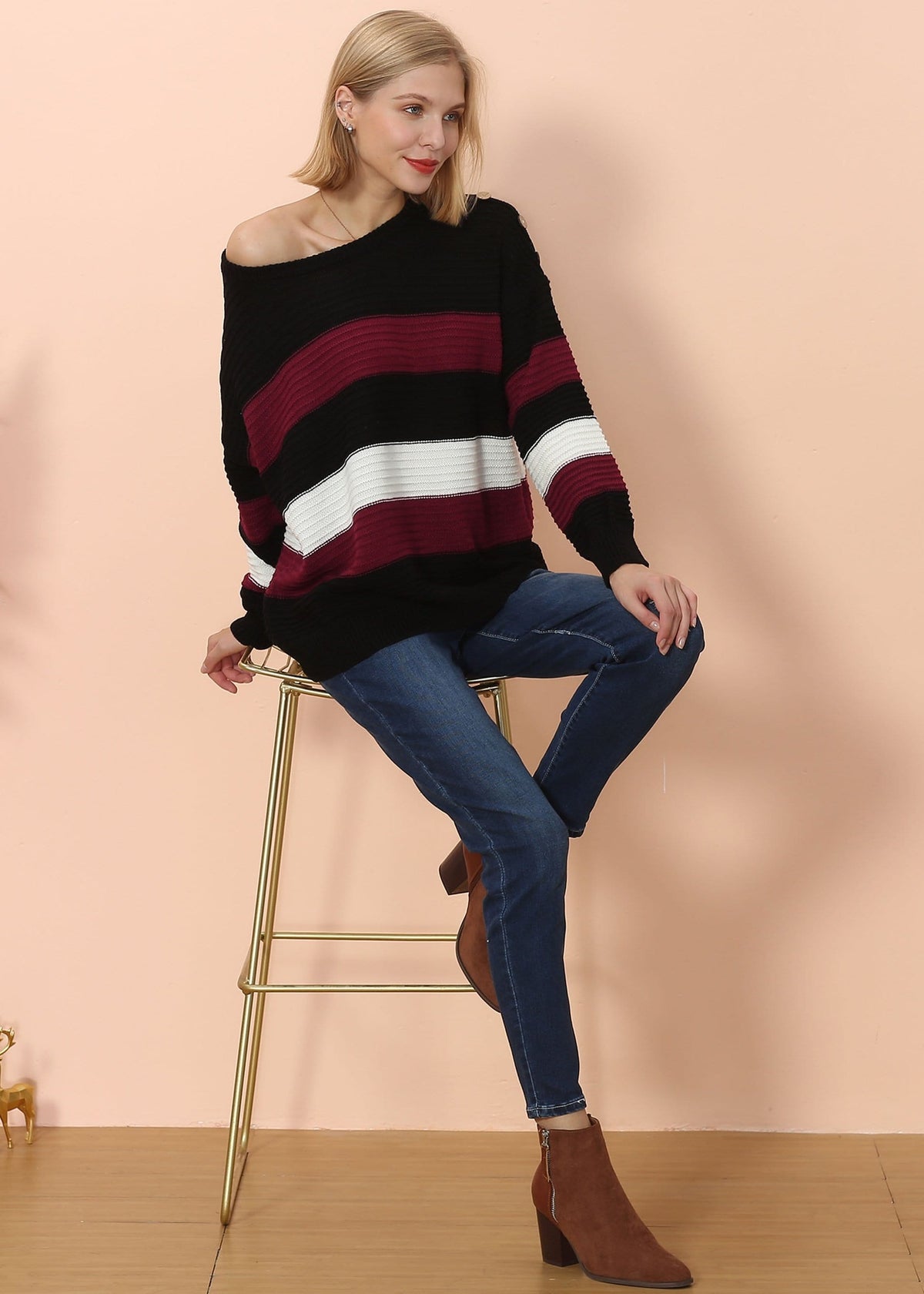Woman wearing a striped sweater and jeans sitting on a stool against a beige background