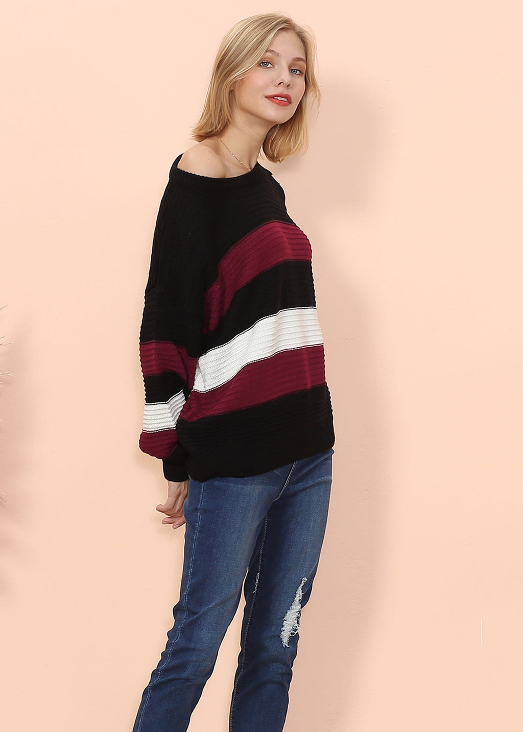 Woman wearing a black, red, and white striped sweater with blue jeans on a pink background