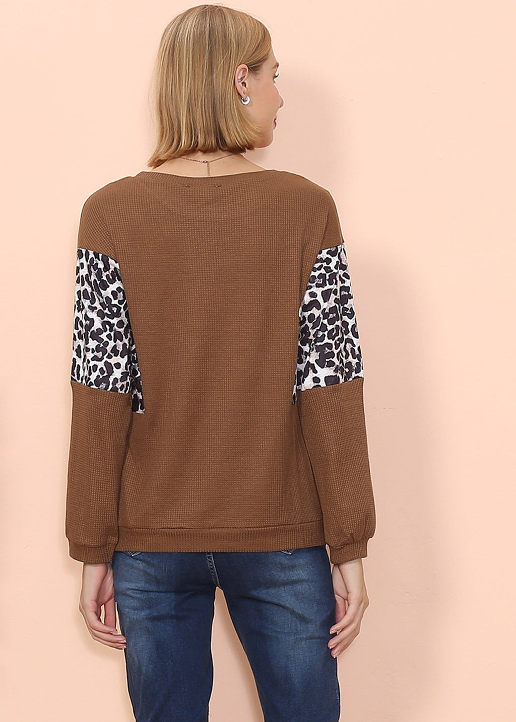 Woman wearing a brown sweater with leopard print sleeves on a beige background