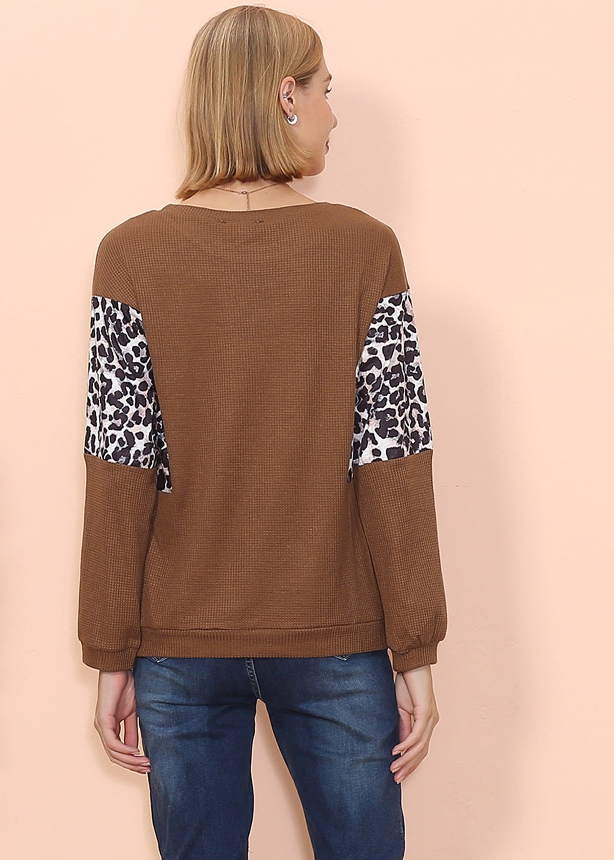 Woman wearing a brown sweater with leopard print sleeves on a beige background