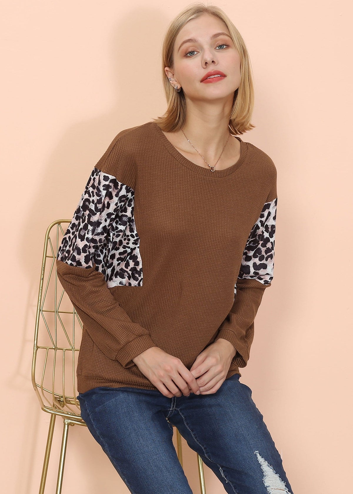 Woman wearing a brown sweater with leopard print sleeves against a beige background