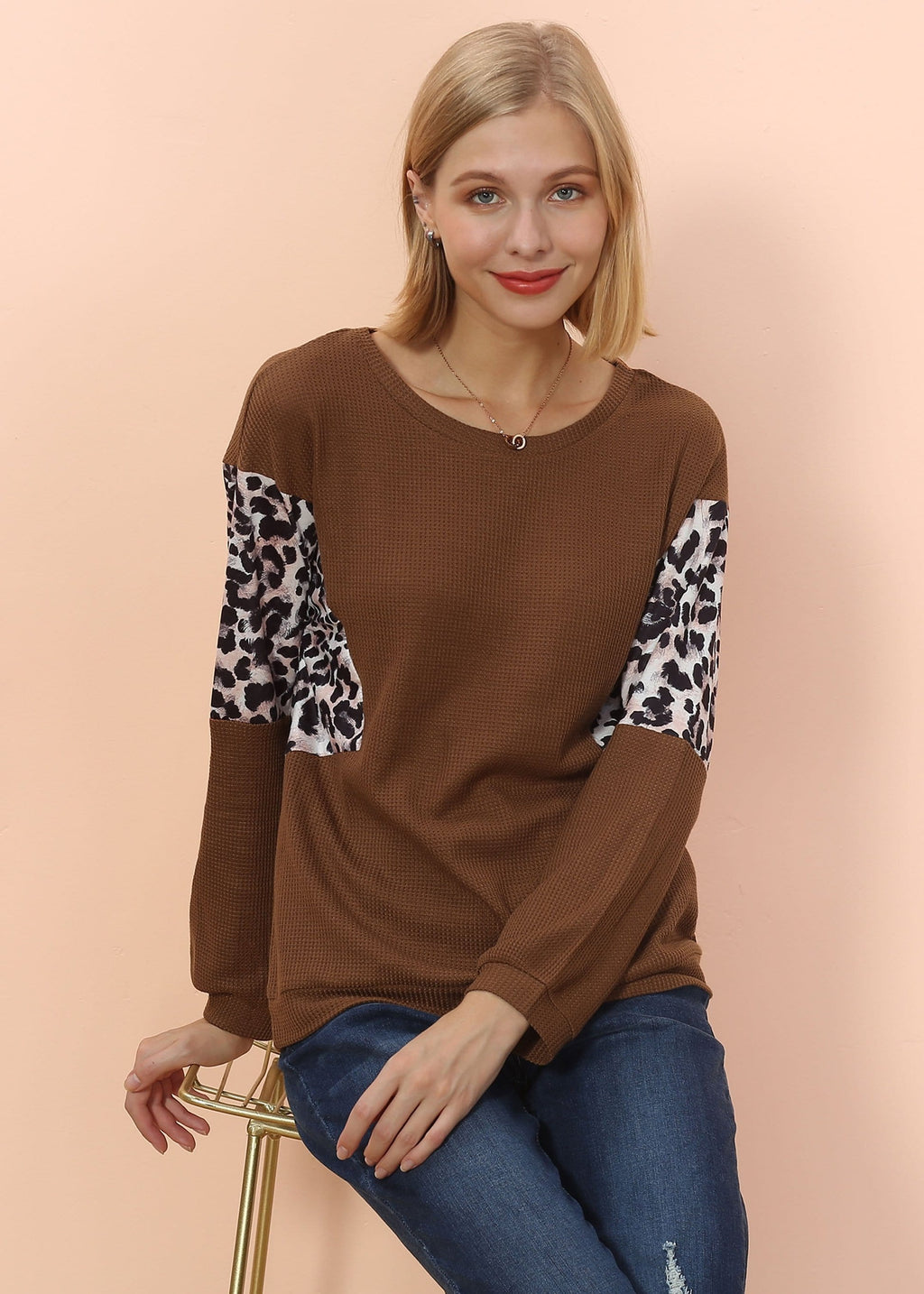 Woman wearing a brown sweater with leopard print sleeves on a peach background
