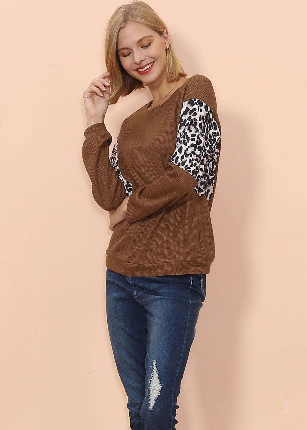 Woman wearing a brown sweatshirt with leopard print sleeves against a beige background