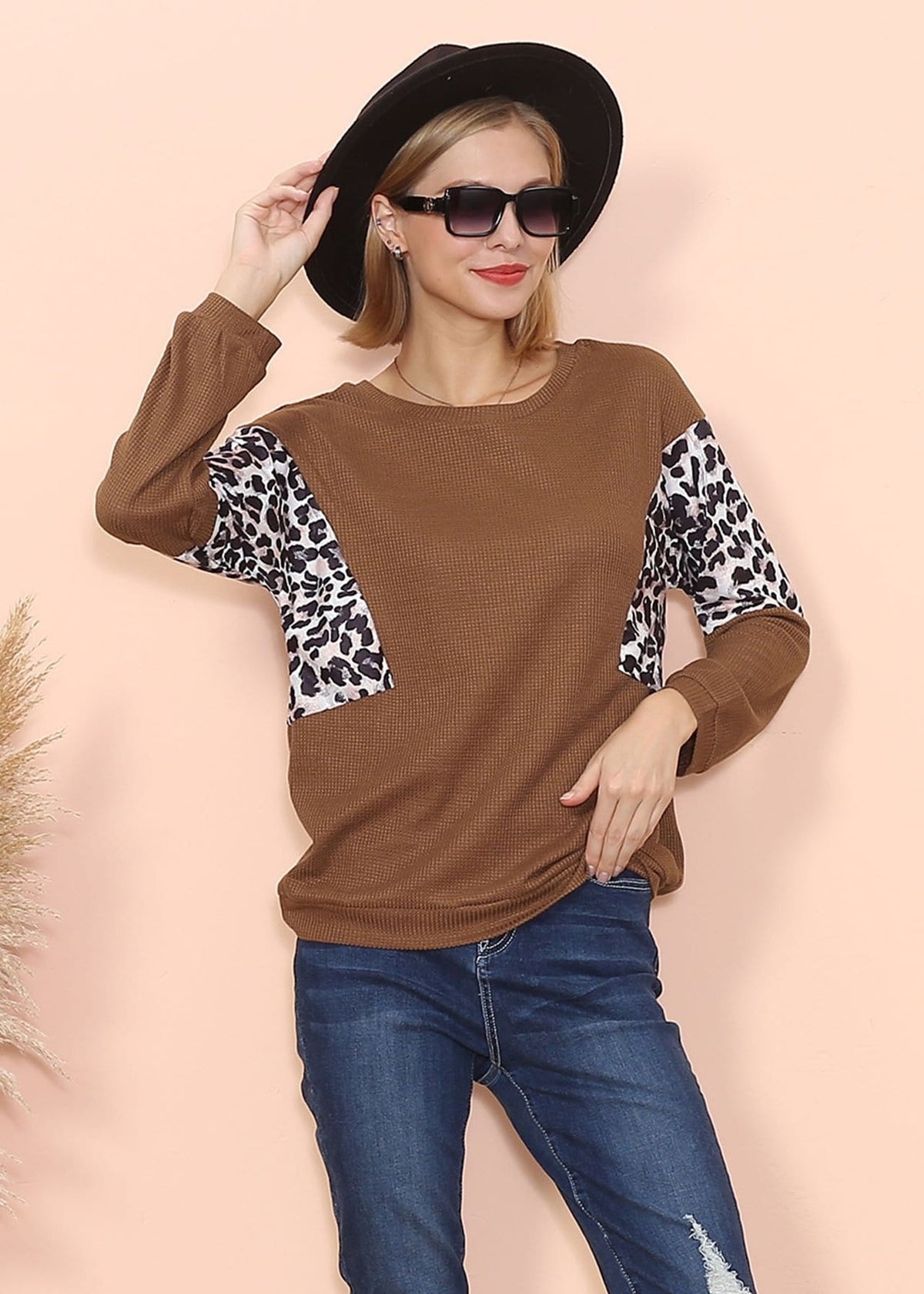 Woman wearing a brown sweater with leopard print sleeves against a beige background
