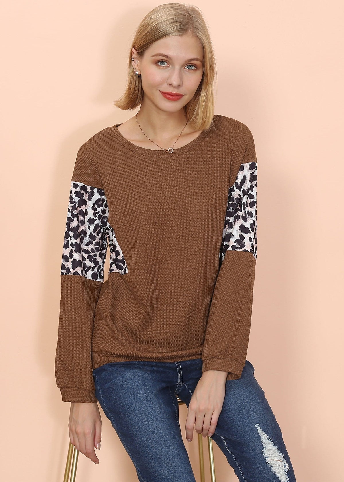 Woman wearing a brown sweater with leopard print sleeves against a beige background