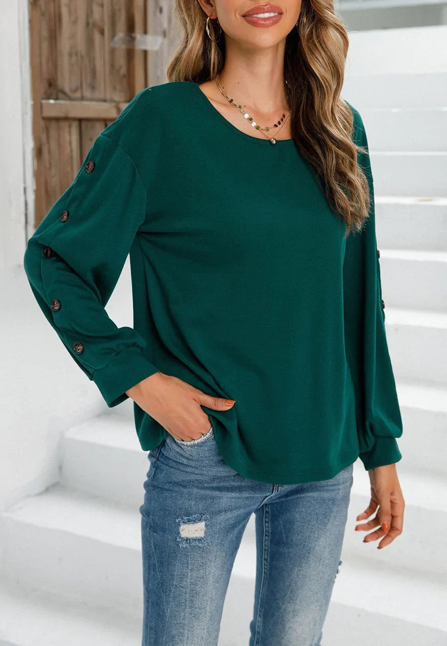 Woman wearing a green long-sleeve top with button details and blue jeans on a white staircase.