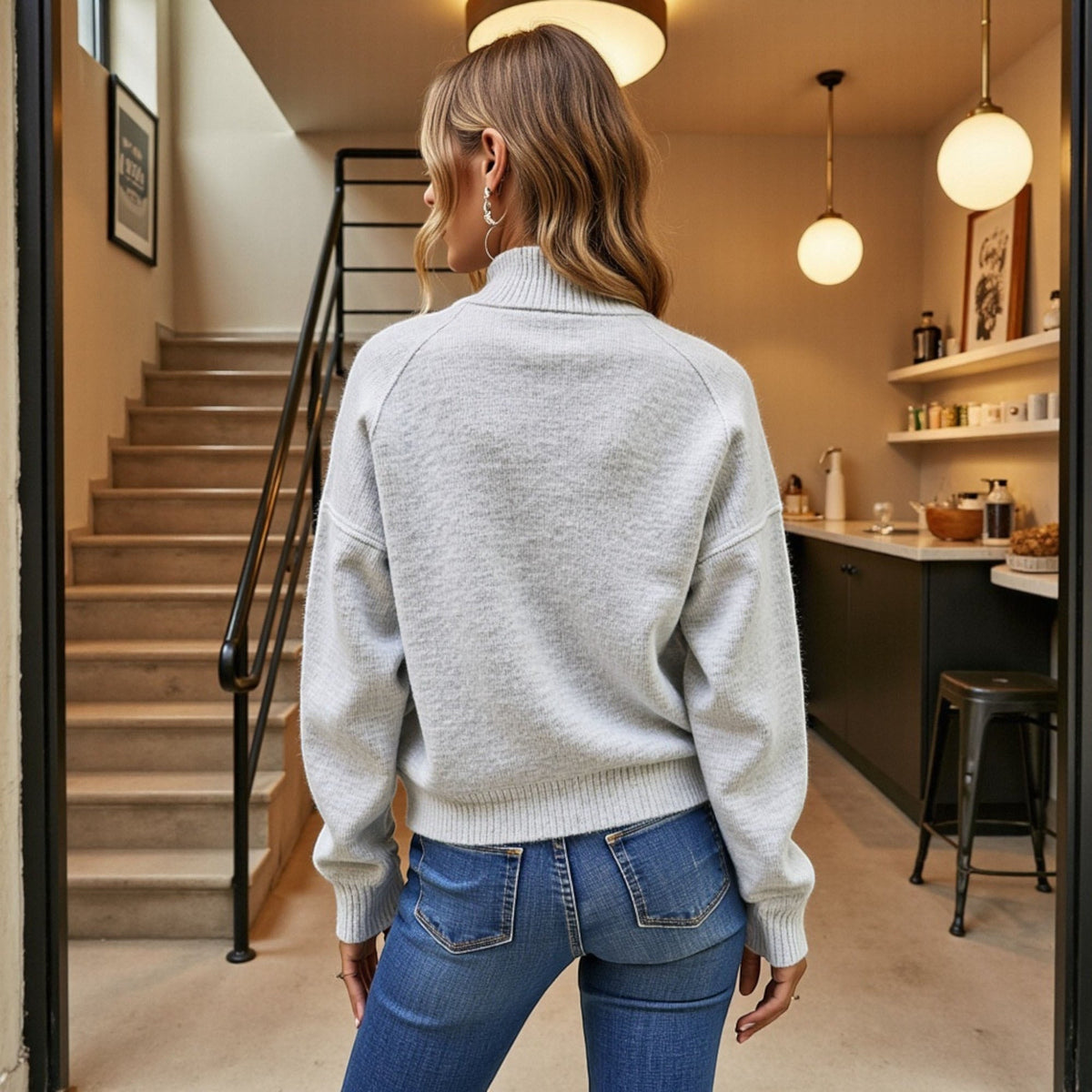 Woman in a gray sweater and blue jeans walking through a modern home interior.