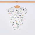 A white short-sleeve baby bodysuit with an all-over whimsical print of cartoon animals, trees, stars, and small objects, hanging on a wooden hanger from a wooden rod against a light gray background.