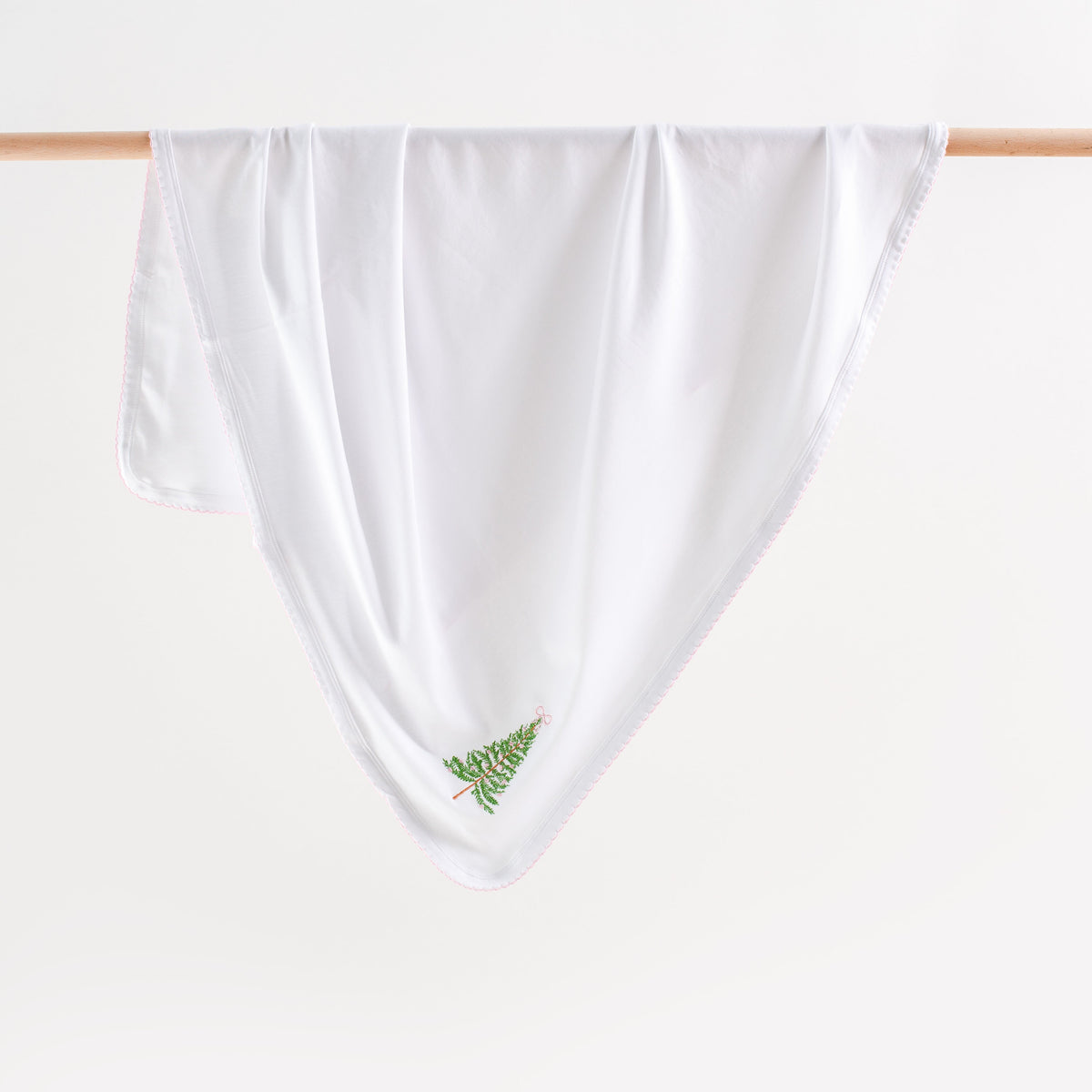 White towel with green leaf design hanging on a wooden rack against a white background