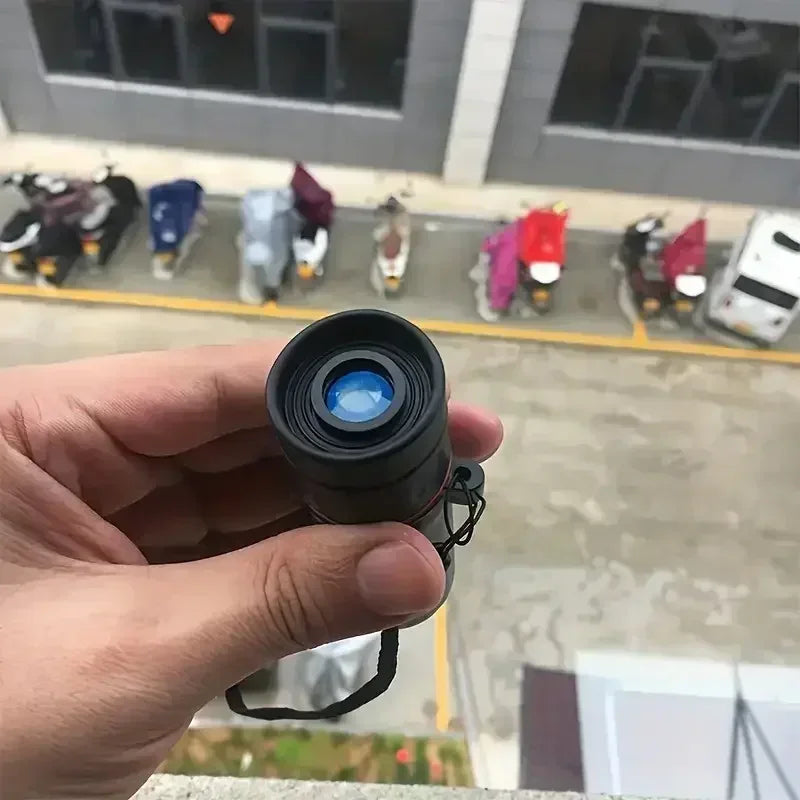 A hand holding a small black cylindrical device with a blue reflective lens, shown against a blurred outdoor background with parked scooters and a building.