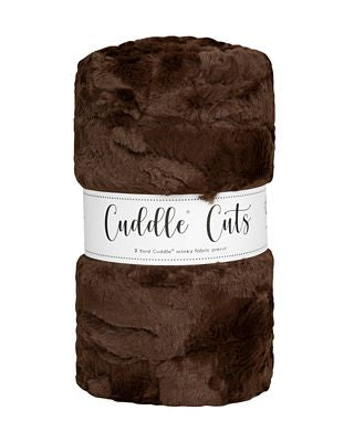 A rolled-up plush faux fur fabric in dark brown with a white paper label wrapped around the middle that reads 'Cuddle Cats'.