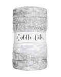 A plush, fuzzy plush fabric rolled into a cylindrical shape with a white paper label band. The blanket has a mottled pattern of light gray, white, and soft silver-gray tones.