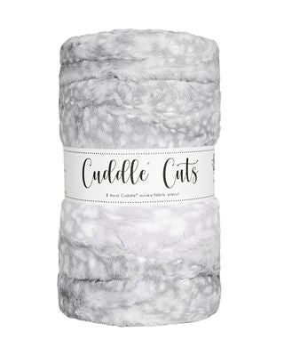 A plush, fuzzy plush fabric rolled into a cylindrical shape with a white paper label band. The blanket has a mottled pattern of light gray, white, and soft silver-gray tones.