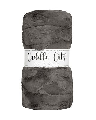 A folded plush faux-fur fabric in dark gray with a white paper label band reading 'Cuddle Cats' on a plain white background.