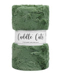 A folded plush faux-fur blanket in a dusty sage green color, wrapped in a white paper band that reads 'Cuddle Cuts'.