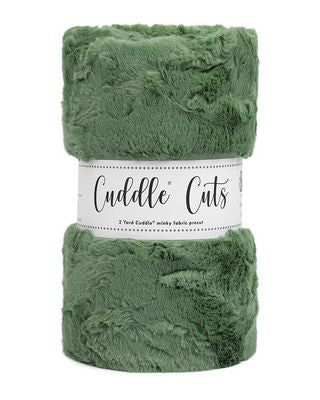 A folded plush faux-fur blanket in a dusty sage green color, wrapped in a white paper band that reads 'Cuddle Cuts'.