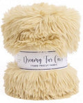 A ball of cream-colored faux fur fabric with a white paper label reading 'Dreamy Fur Co 1 Yard Precut Fabric' on a white background.