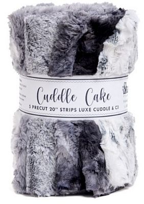 A  plush faux-fur fabric in mixed gray, white, and black tones, wrapped with a paper band labeled 'Cuddle Cake'.
