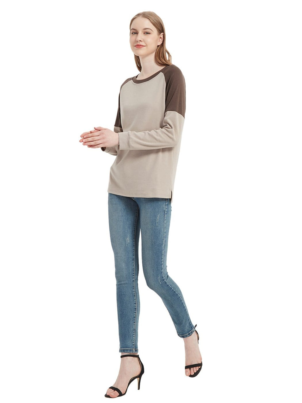 Woman wearing a beige and brown long-sleeve top with blue jeans on a white background