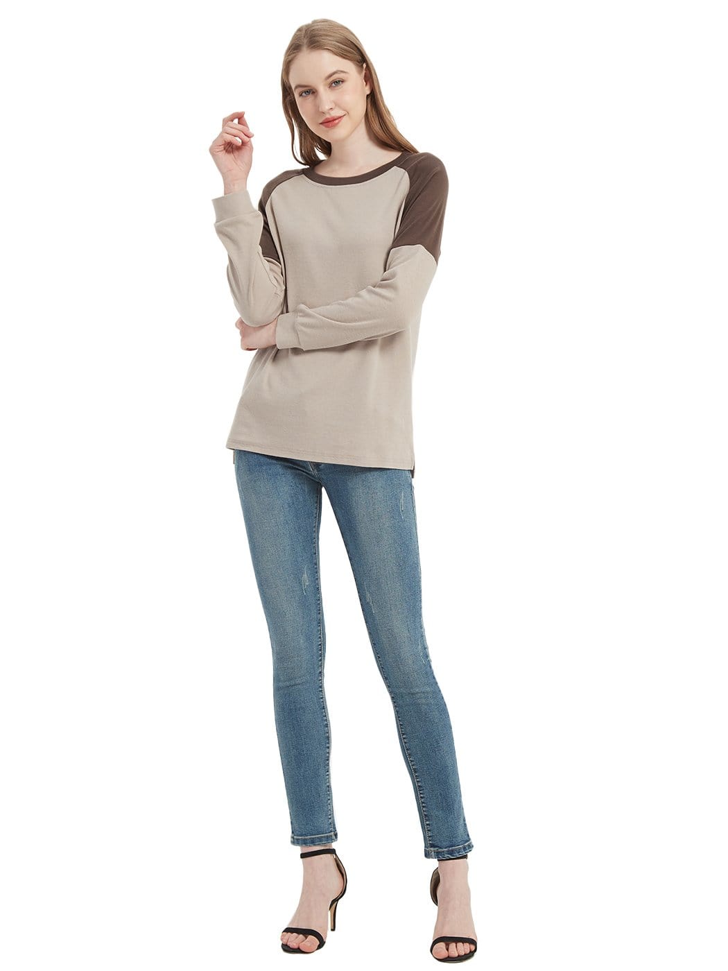 Woman wearing a beige and brown long-sleeve top with blue jeans on a white background