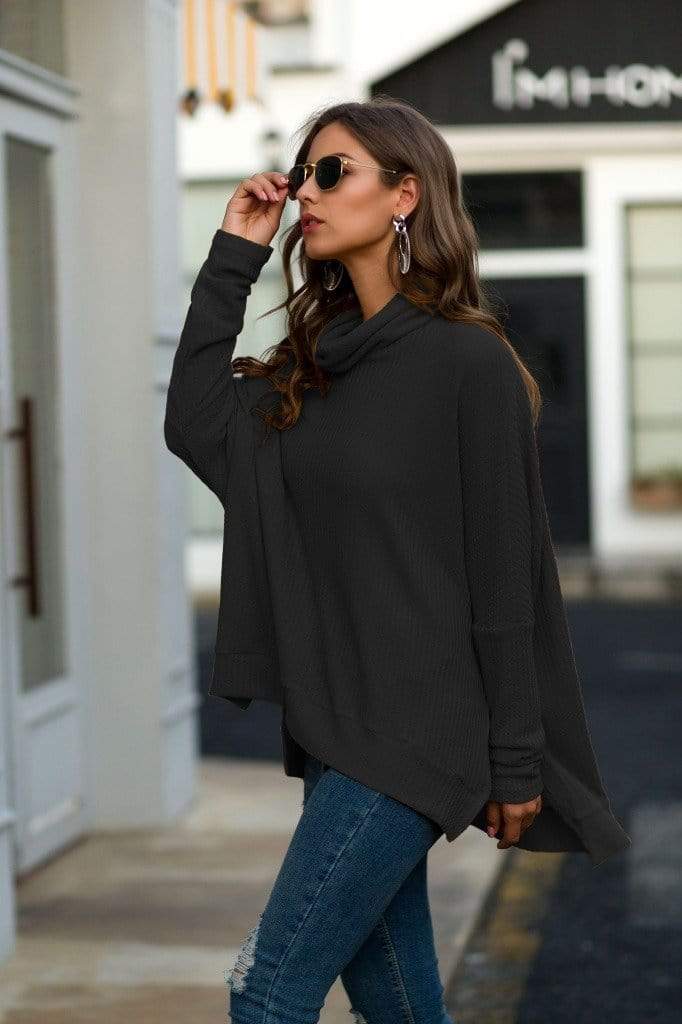 Woman wearing a black oversized sweater and blue jeans on a city street.