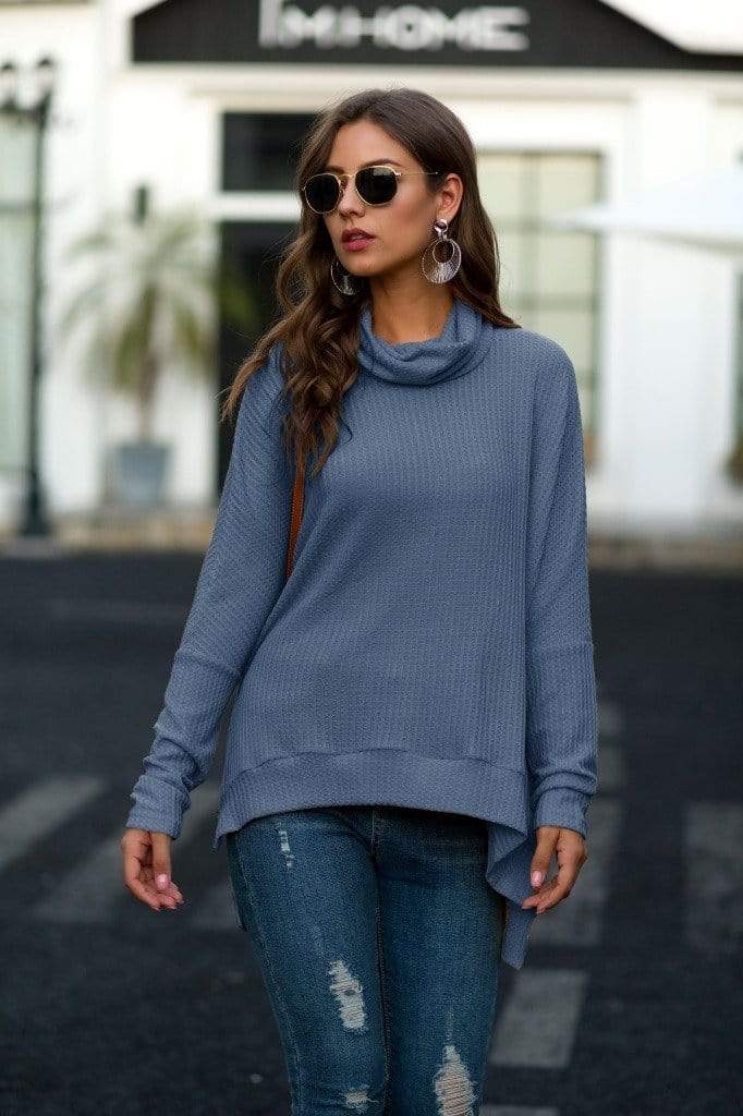 Woman wearing a blue sweater and jeans on a street.