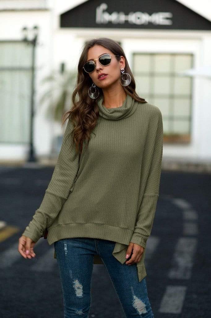 Woman wearing an olive green sweater and blue jeans outdoors.