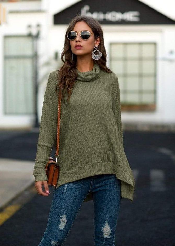 Woman wearing an olive green sweater and blue jeans with a blurred background