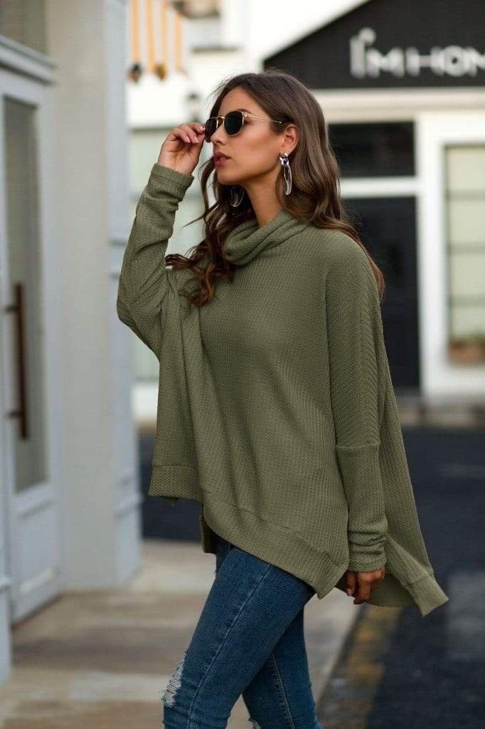 Woman wearing a green sweater and blue jeans on a city street.
