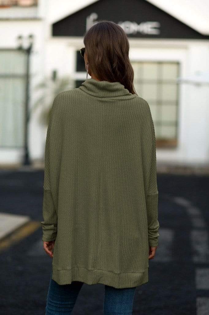Person wearing an olive green sweater with a blurred background